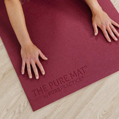 Red yoga mat with 'The Pure Mat by Pure Practice' branding on a wooden floor.